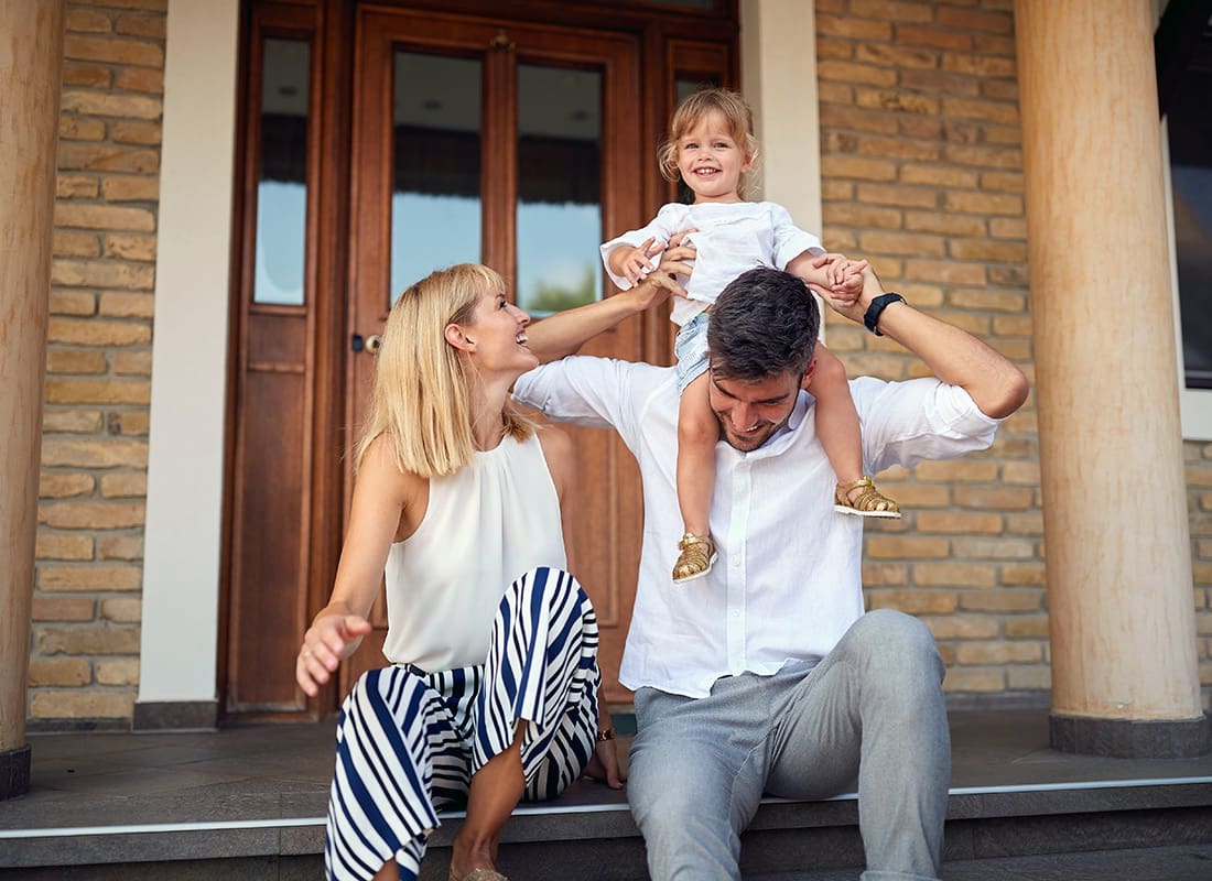 Personal Insurance - Portrait of a Cheerful Mother and Father Having Fun Sitting on the Front Steps of Their Home While Playing with Their Daughter